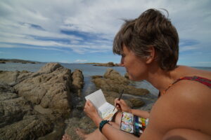 Giulia Razetti, an illustrator from Turin, sketching live in a notebook during a trip to the beach.