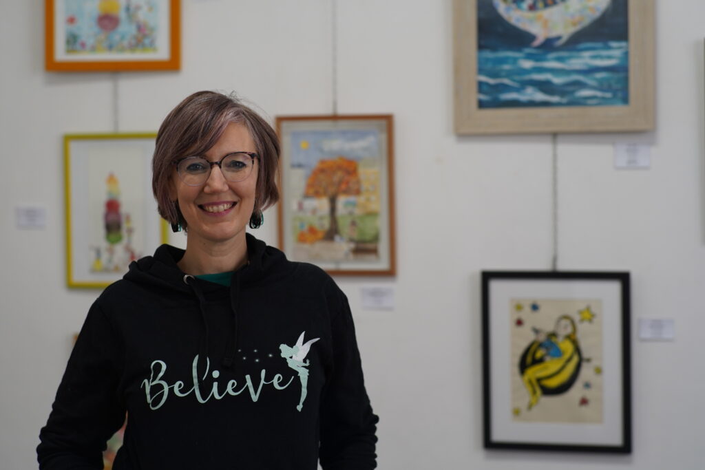 A portrait of Giulia Razetti, an illustrator in Turin, smiling in front of her artwork in an art gallery.