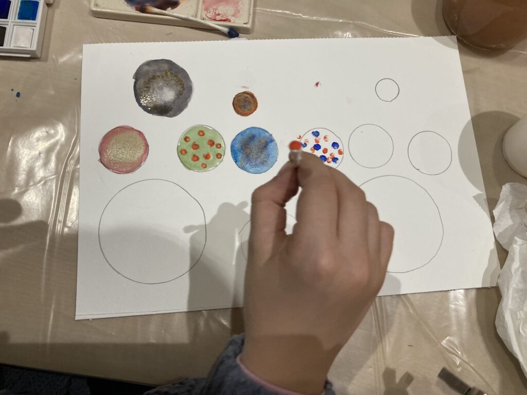A close-up of a child's hand using a brush to fill in drawn circles, learning watercolor techniques and creating colorful bubbles.