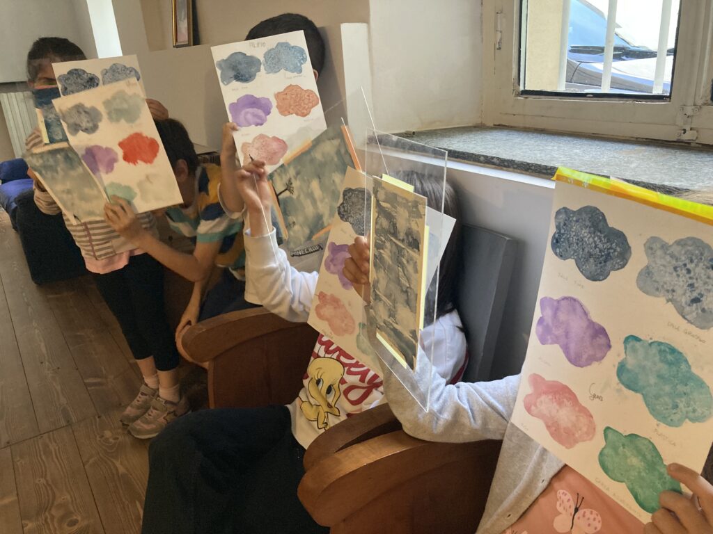 A group of children in an art workshop showing off their colorful cloud drawings, created using watercolors and stencils.